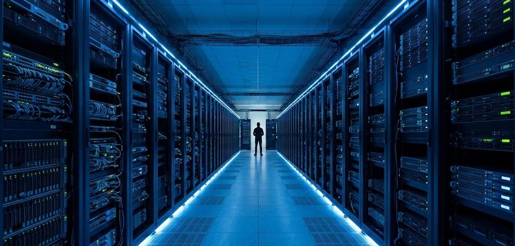 Silhouetted figure in a vast blue-lit data center — AI and business automation